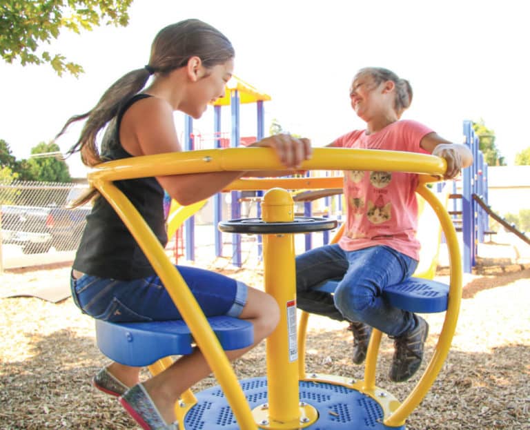 two girls laughing and spinning on playground equipment